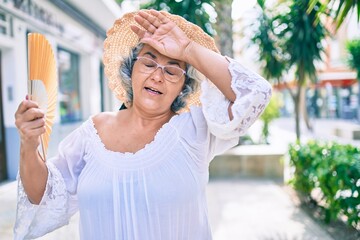 Poster - Middle age woman with grey hair using handfan on a very hot day of a heat wave