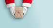© eggeeggjiew - Top view of Santa claus hands is holding a brown gift box or present box over blue isolated background.