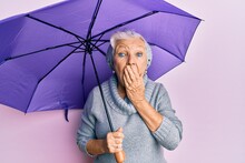 Senior Grey-haired Woman Holding Purple Umbrella Covering Mouth With Hand, Shocked And Afraid For Mistake. Surprised Expression