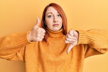 Poster - Beautiful redhead woman wearing casual winter sweater over yellow background doing thumbs up and down, disagreement and agreement expression. crazy conflict