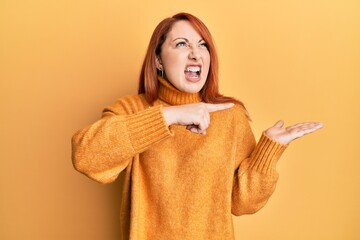 Wall Mural - Beautiful redhead woman pointing with finger to empty space on open palm angry and mad screaming frustrated and furious, shouting with anger. rage and aggressive concept.