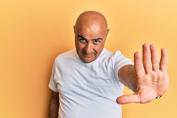 Mature middle east man wearing casual white tshirt doing stop sing with palm of the hand. warning expression with negative and serious gesture on the face.