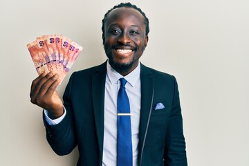 Poster - Handsome young black man holding south african rand banknotes looking positive and happy standing and smiling with a confident smile showing teeth