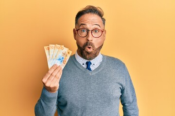 Poster - Handsome middle age man holding swiss franc banknotes scared and amazed with open mouth for surprise, disbelief face