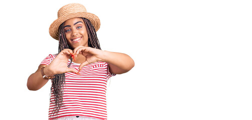 Sticker - Young african american woman with braids wearing summer hat smiling in love doing heart symbol shape with hands. romantic concept.