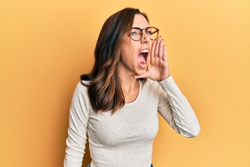 Canvas Print - Young brunette woman wearing casual clothes and glasses shouting and screaming loud to side with hand on mouth. communication concept.