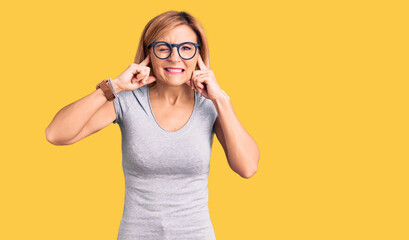 Wall Mural - Young blonde woman wearing casual clothes covering ears with fingers with annoyed expression for the noise of loud music. deaf concept.