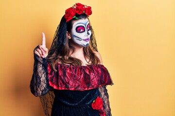 Sticker - Young woman wearing day of the dead costume over yellow pointing finger up with successful idea. exited and happy. number one.