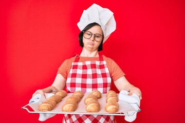 Canvas Print - Brunette woman with down syndrome wearing baker uniform holding homemade bread relaxed with serious expression on face. simple and natural looking at the camera.