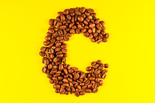 Latin alphabet letters made with coffee beans on yellow background
