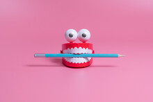 A Plastic Toy In The Form Of Red Jaws With White Teeth And Eyes Holds A Pencil Between Its Teeth. Copywriting Concept