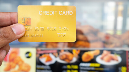 Hand holding the credit card with fried chicken shop in background.16:9 style