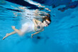 © alexbard - Happy naughty little girl looks at the camera while swimming underwater in a children's pool in a white dress on a blue background. The concept of happiness. Portrait. Horizontal orientation