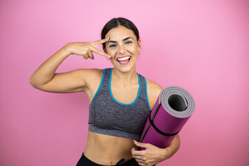 Young beautiful woman wearing sportswear over isolated pink background Doing peace symbol with fingers over face, smiling cheerful showing victory. Holding a splinter in her hand.