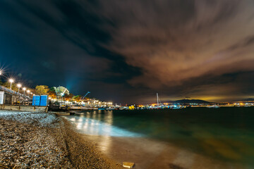 Wall Mural - Sea coast with reflection of city lights in the water. Gelendzhik promenade and beach at night.