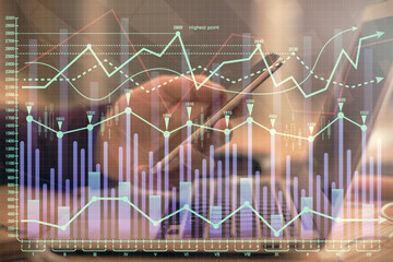 Double exposure of man's hands holding and using a phone and financial graph drawing. Analysis concept.