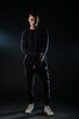 © qunica.com - Full-length picture of an attractive sexy young male model posing isolated on a black background and wearing black blouse and black pants.