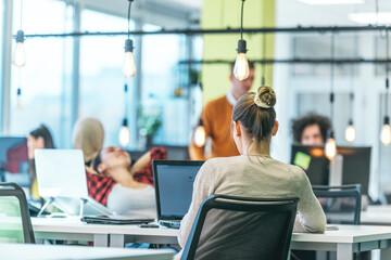 Blonde businesswoman working on her pc while sitting in a crowded modern office.