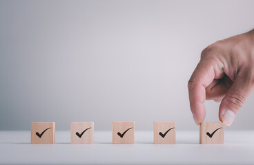 Checklist Survey and assessment concept, human hand putting cube wood with Check mark icon on wooden blocks, gray background with copy space