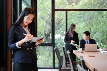 Young busineswoman using stylus pen writing on digital tablet while standing in her office.