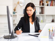 © JackF - Smiling woman working with papers and laptop in office