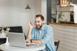 © ViDi Studio - Surprised young man sitting alone at table in coffee shop cafe working studying on laptop pc computer hold pen relaxing in restaurant during free time indoor. Freelance mobile office business concept.