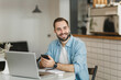 © ViDi Studio - Handsome young man sitting at table in coffee shop cafe restaurant indoors working studying on laptop pc computer listening music with air pods cell phone. Freelance mobile office business concept.