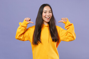 Wall Mural - Cheerful funny pretty attractive young brunette asian woman 20s in casual yellow hoodie standing pointing thumbs on herself looking camera isolated on pastel violet colour background studio portrait.