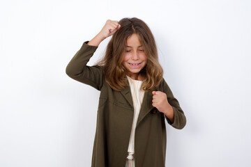 Wall Mural - Attractive Beautiful little girl standing against white background, celebrating a victory punching the air with his fists and a beaming toothy smile.