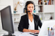 Office worker woman is working at a computer and talking by headset with client in the office