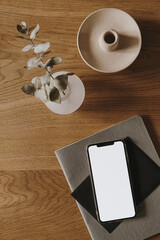 Wall Mural - Flatlay of blank screen smart phone, notebook, eucalyptus branch on wooden background. Home office desk workspace. Business, work template. Flat lay, top view.