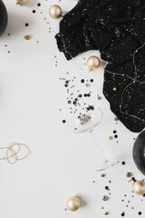 Poster - Christmas / New Year holiday celebration concept. Gold, black confetti, champagne glass, female dress on white background. Flatlay, top view.