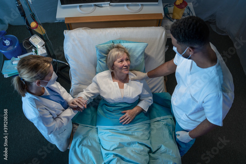 Obraz na płótnie Top view of cheerful doctors and covid-19 patient in bed in hospital, coronavirus and recovery concept.