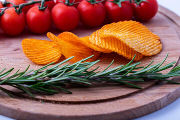 Potato chips with a sprig of rosemary and cherry tomatoes on a wooden table.