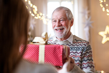 Senior man giving present to unrecognizable woman indoors at home at Christmas.