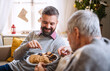 © Halfpoint - Mature man and senior father indoors at home at Christmas, eating biscuits.