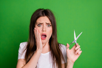 Sticker - Photo portrait of upset girl holding scissors touching face with one hand open mouth isolated on vivid green colored background