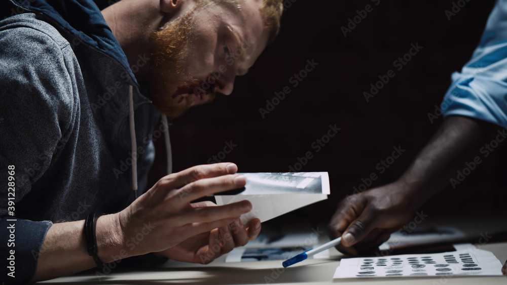 Close up of beaten arrested man negotiating with detective during interrogation - obrazy, fototapety, plakaty 