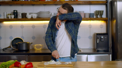 Young bearded man crying chopping onion in kitchen at home