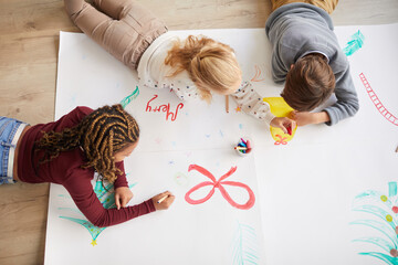 top view at multi-ethnic group of kids drawing pictures on floor while enjoying art class on christm