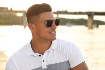 Wall Mural - Handsome man wearing stylish sunglasses near river