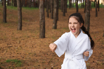 Cute little girl in kimono practicing karate in forest