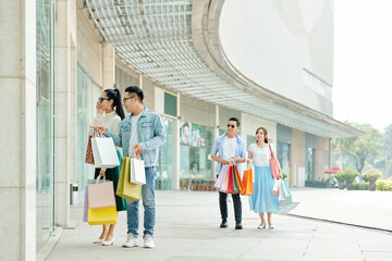 Sticker - Excited young people with paper-bags looking at stylish clothing item in shop window