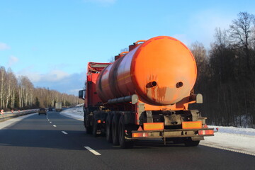 Modern orange fuel truck with semi trailer tanker barrel drive on suburban highway road at Sunny winter day in perspective on blue sky and bare treees background, rear side view - ADR dangerous cargo