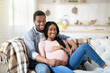 © Prostock-studio - Beautiful pregnant couple hugging on sofa at home