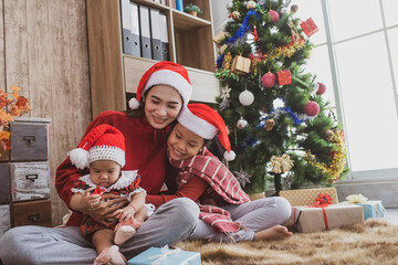 Canvas Print - parent and two little children having fun and playing together near christmas tree indoors. merry christmas and happy holidays. cheerful mom and her cute daughters girls exchanging gifts.