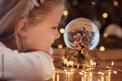Cuadros en Lienzo Girl looking at a glass ball with a scene of the birth of Jesus Christ in a glas