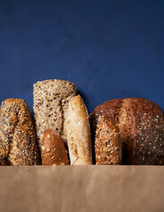 Bread bakery background. Assortment of baked bread brown and white wheat grain loaves in crafting the package on a Blue classic background. Copy space. Top view.