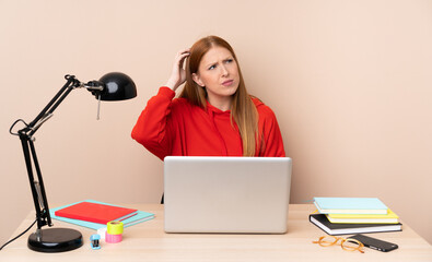 Young student woman in a workplace with a laptop having doubts while scratching head