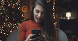 Fototapeta Tulipany - Happy woman using her smartphone on Christmas day